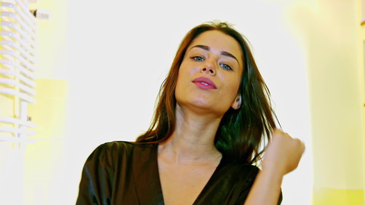 Beautiful long hair. A young woman stands in the bathroom and combs her hair. Hair care concept. The brunette looks at the camera and touches her hair