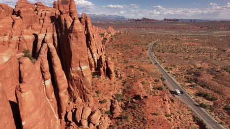 Red-rock-formations-rise-alongside-a-winding-road-through-the-vast-desert-landscape-of-Moab,-Utah-USA