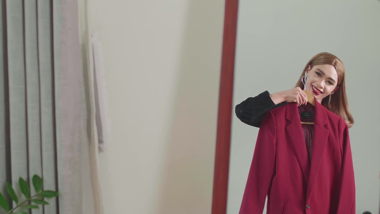 Young Transgender Woman Choosing Clothes To Wear In Front Of Mirror In Interior