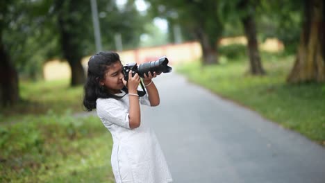 a cute little asian girl is taking photos of nature and trees in a jungle with a digital slr camera like a professional photographer