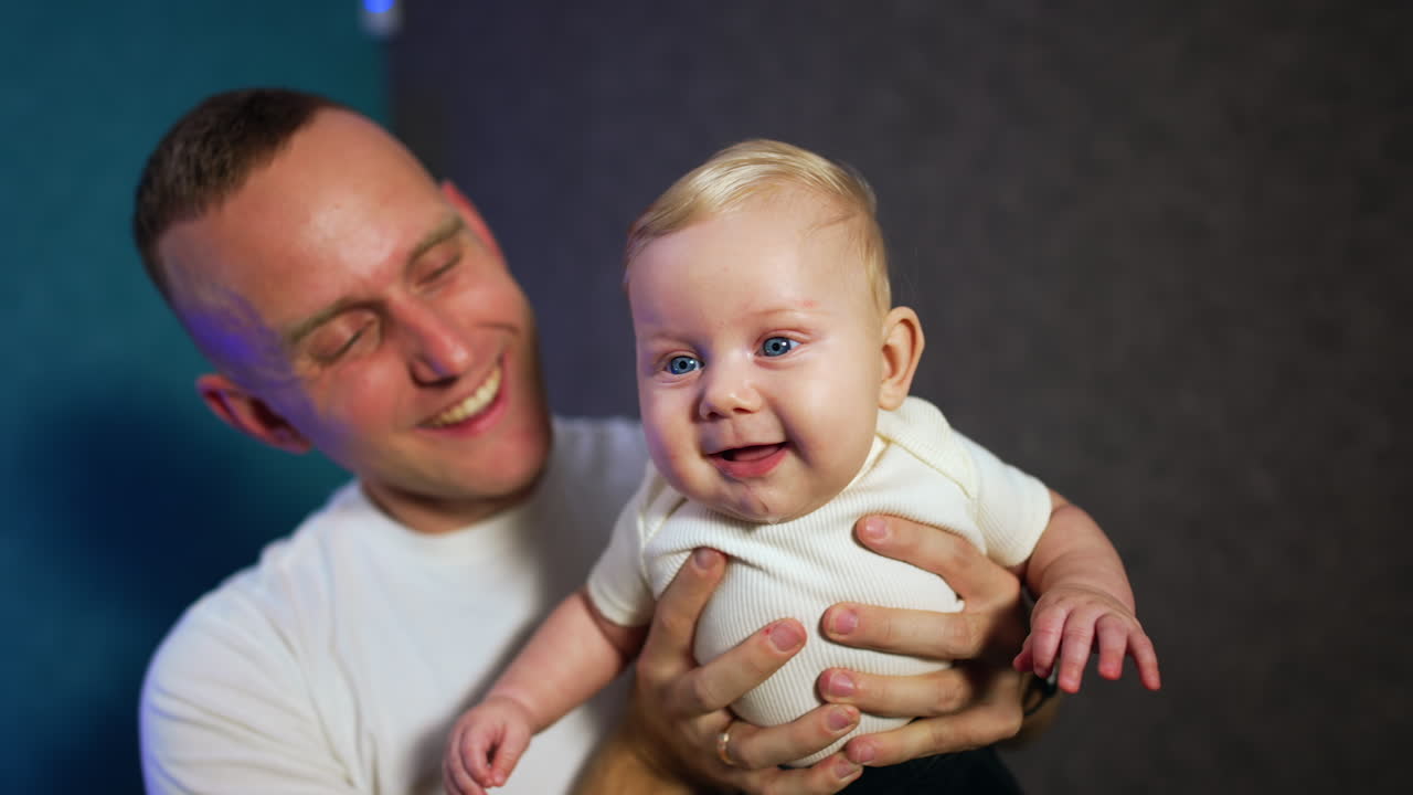 Loving father holding his adorable blond infant son. Dad with his baby smiling sweetly to camera.