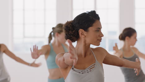 beautiful yoga woman practicing warrior pose in fitness studio hispanic female training with instructor group of women enjoying healthy balanced lifestyle