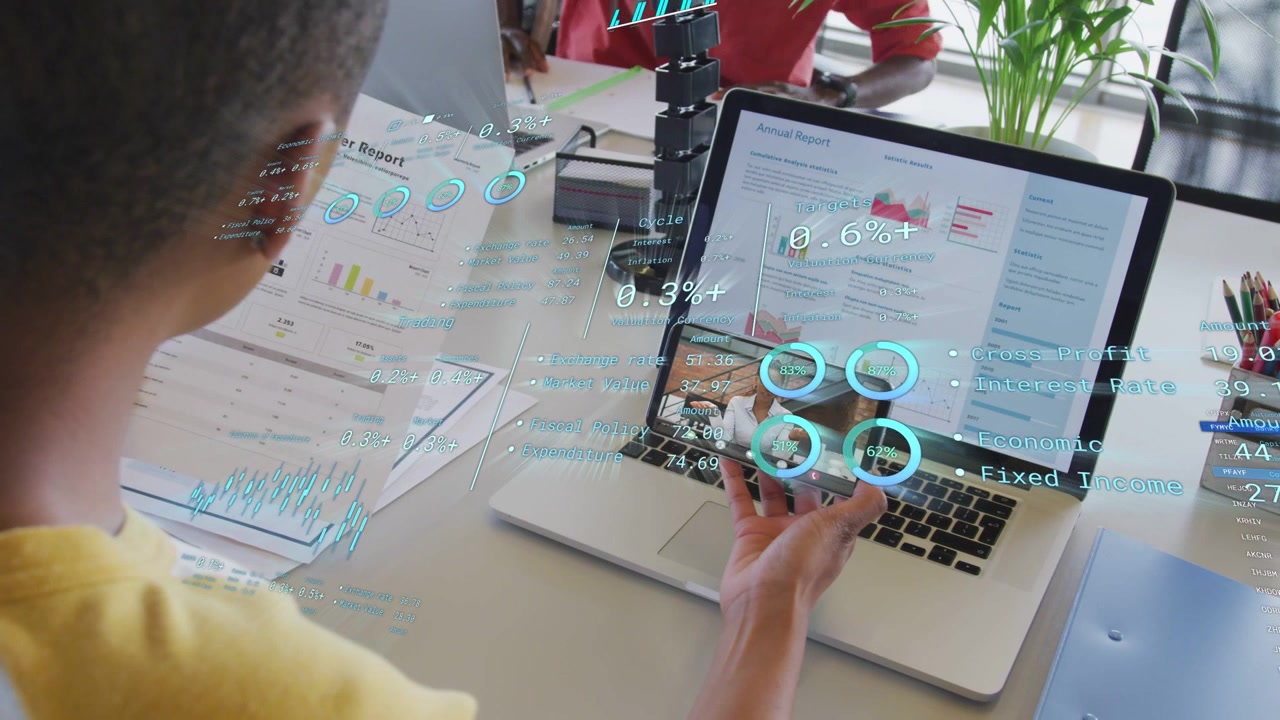 Data analyst holding phone over laptop, shifting phone while AR charts updating, peer gesturing