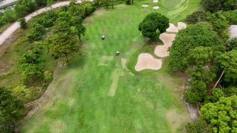 drone footage captures golfers on a lush, green course in phuket, thailand, showcasing vibrant landscapes and strategic sand bunkers