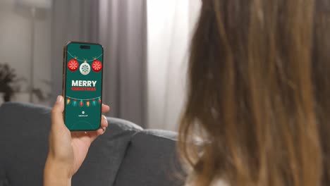 primer plano de una mujer sentada en el sofá en casa mirando las ofertas en línea de navidad en el teléfono móvil 1