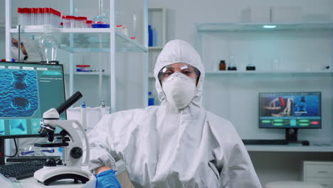 tired microbiologist in coverall sitting in laboratory looking at camera