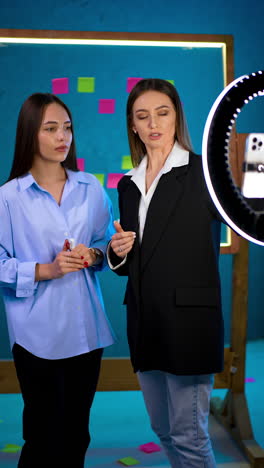 women working at video creation. ladies look at phone on tripod and ring light before footage. vertical video.