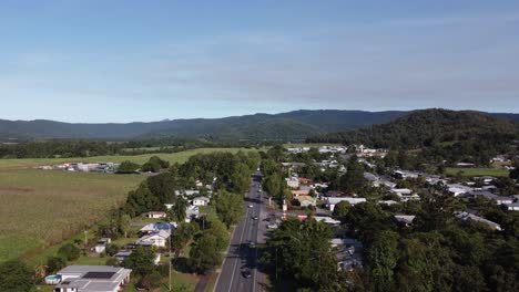 drone ascending over a country town road revealing sugarcane plantations near by and a highway in north queensland, australia