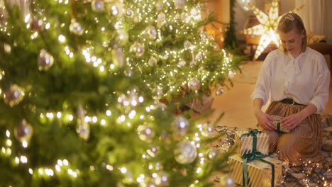 woman wrapping presents by christmas tree in beautiful modern very exclusive decorated house