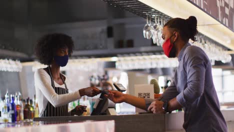 Mixed-race-man-giving-african-american-female-cafe-worker-his-credit-card-in-order-to-pay