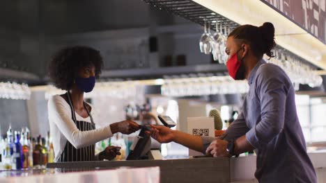 hombre de raza mixta dando a una trabajadora de café afroamericana su tarjeta de crédito para pagar