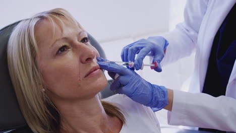 mature woman sitting in chair being give botox injection by female doctor