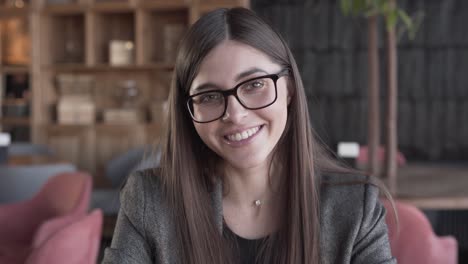 close-up portrait of a beautiful girl in glasses with natural make-up looking at camera and smiling pleasantly