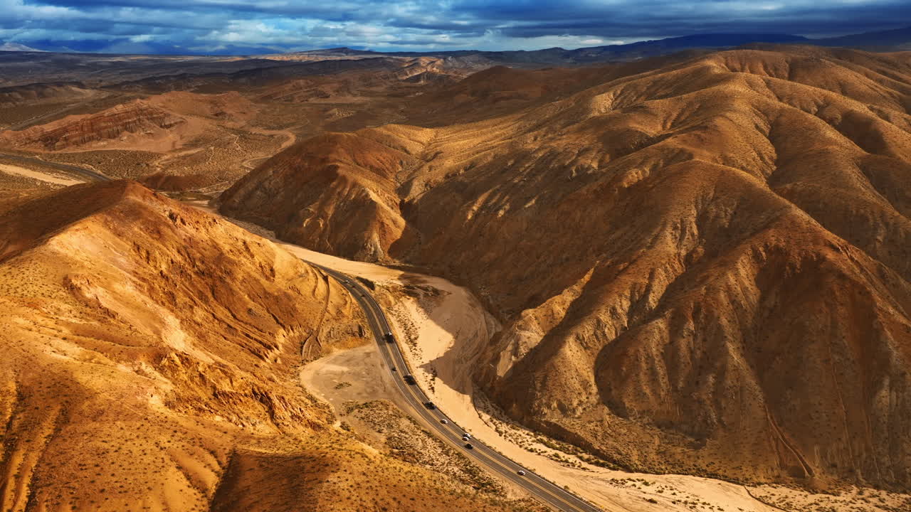Highway with moving cars in the valley among the gorgeous mountains. Rocky landscape of Nevada, USA at sunset from aerial view.