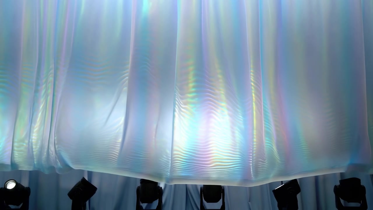 Time-lapse sequence of translucent iridescent fabric descending and settling over metallic pleated backdrop, begins billowing near top-center with gentle
