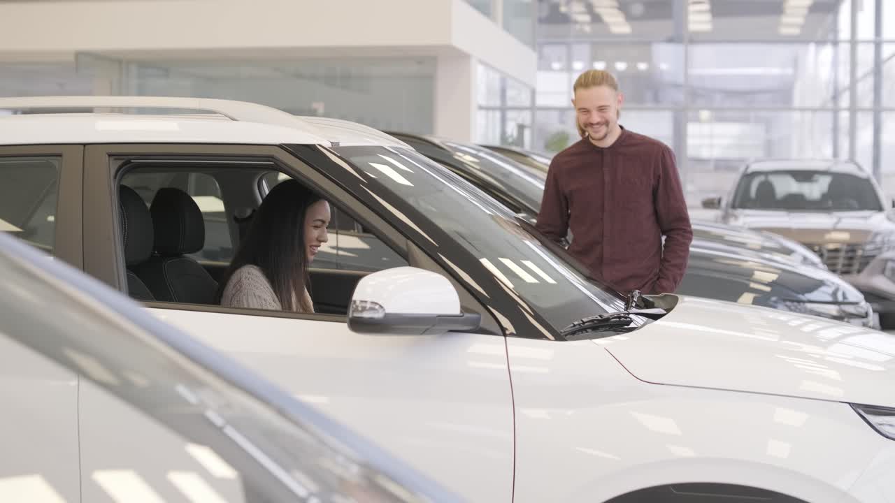 una hermosa pareja de jóvenes en la sala de exposición de automóviles eligiendo un coche nuevo para comprar.