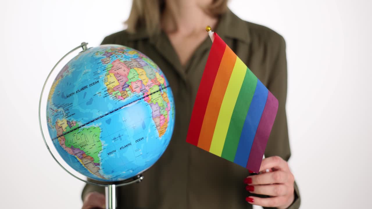 Donna tiene un mappamondo e una bandiera LGBT pride su sfondo bianco