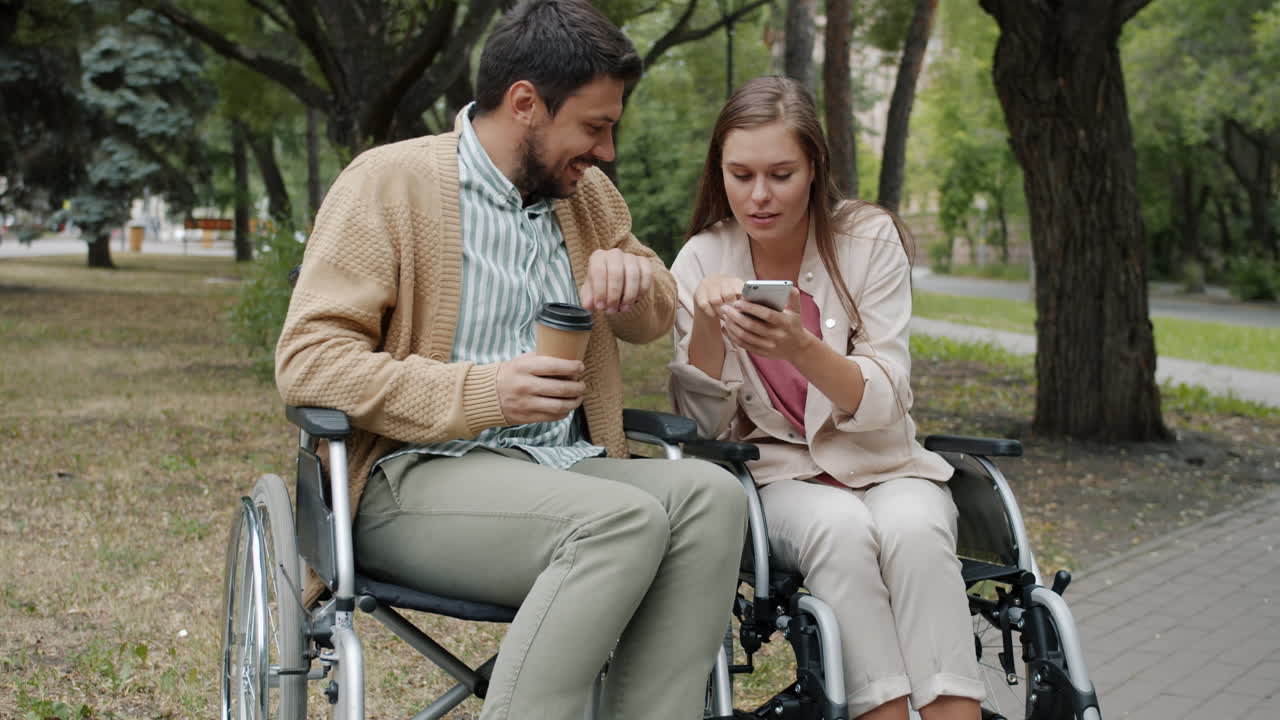 Couple in Wheelchairs Enjoying Coffee and Smartphone in a Park