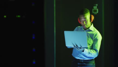 técnico informático afroamericano que usa una computadora portátil trabajando en una sala de servidores de negocios