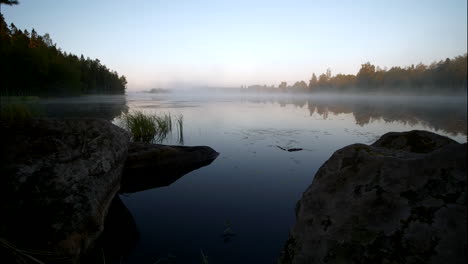 Sunrise-time-lapse-at-lake-with-morning-mist-overlooking-Lund-village,-Sweden