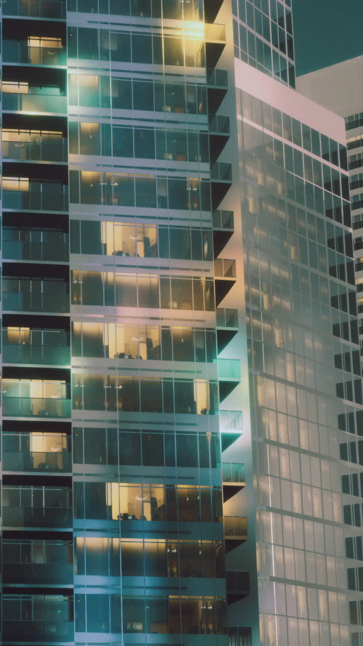 Rascacielos de la ciudad de noche con ventanas iluminadas que muestran la vida interior.