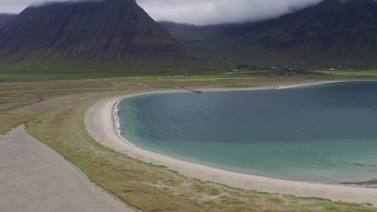 Aerial wide shot of Onundarfjordur Beach with gigantic mountain range and blue lagoon water on Iceland