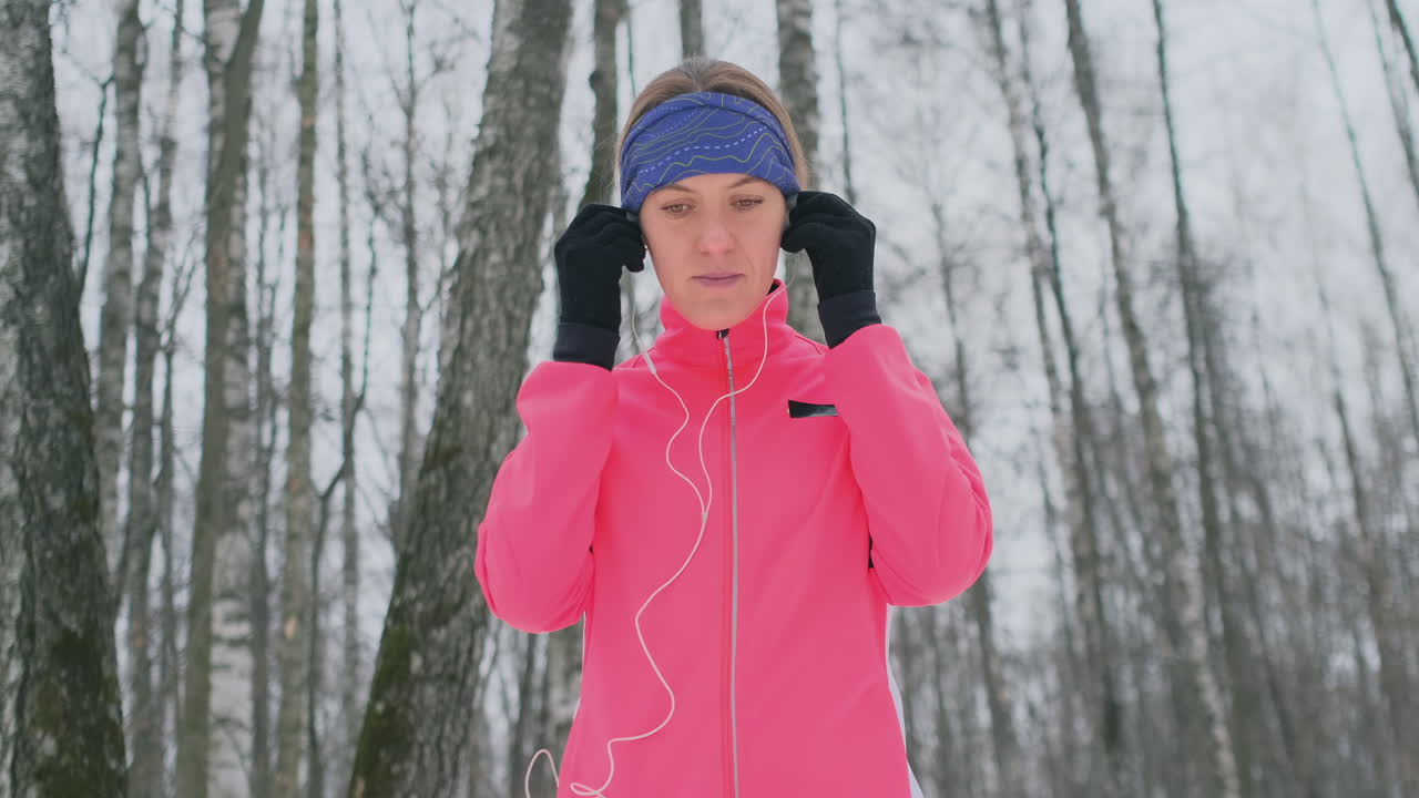 The female before the morning winter jog inserts headphones in the ears and is preparing to run through the natural Park in slow motion.