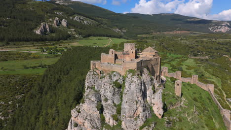 drone orbiting an ancient stone castle perched on a rocky cliff, with panoramic views of green hills and forests under a blue sky. captured in high-resolution during daylight