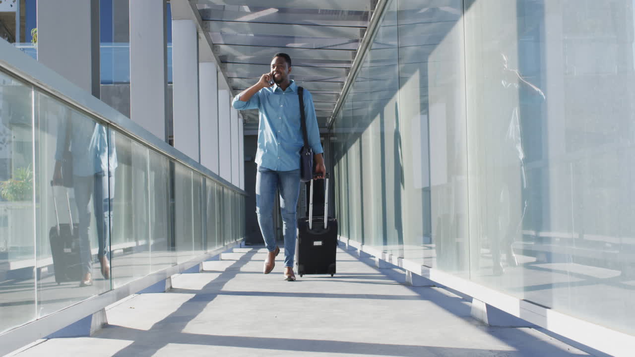 Video of african american man walking with suitcase and using smartphone