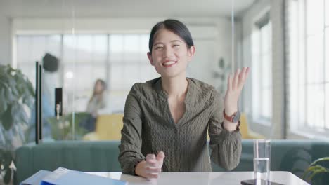 portrait of happy asian casual businesswoman waving during video call in office, slow motion