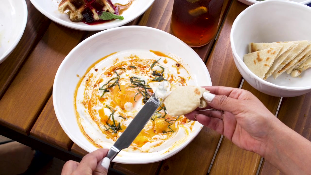 Persona che mangia uova turche Cilbir con pane pita e coltello, uovo in camicia in salsa di yogurt al burro speziato gustato