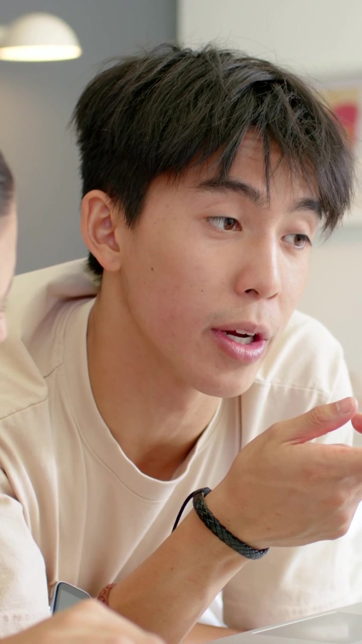 Video verticale: Un'altra persona che indica, uomo asiatico che si appoggia, ascolta e risponde a casa, con braccialetto.