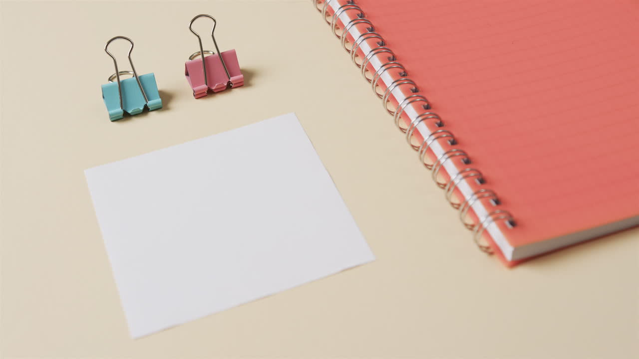 primer plano de un cuaderno rojo y artículos escolares dispuestos sobre un fondo beige, en cámara lenta