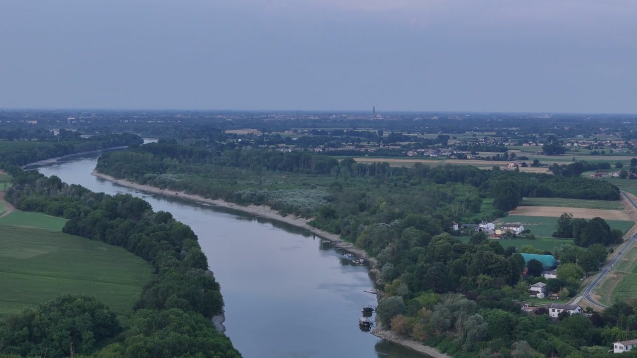 Fiume Po vicino a Isola Serafini, Monticelli d'Ongina, Piacenza, Emilia-Romagna, Italia, che rivela lo skyline distante di Cremona e il Torrazzo sopra la pianura alluvionale durante l'ondata di calore del 2026, ascesa del drone.