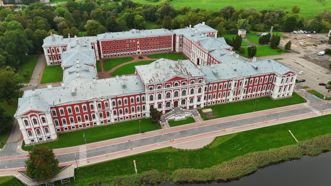 Jelgava Palace designed by Rastrelli with red and white facade grey roof and riverfront layout showing baroque symmetry and landscape integration in central Latvia, Drone establishing shot
