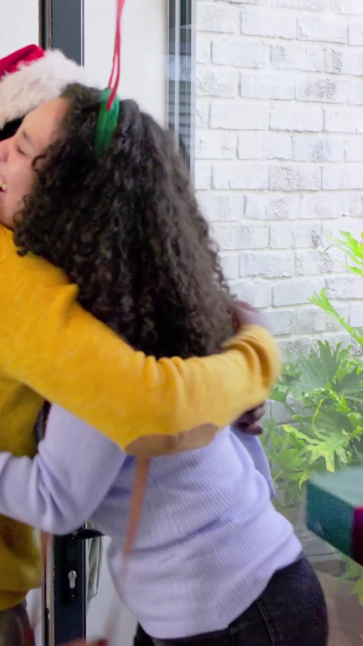 Video verticale: Porta che si apre, donna con le corna abbraccia i padroni di casa per una visita festiva a casa, consegnando un regalo.