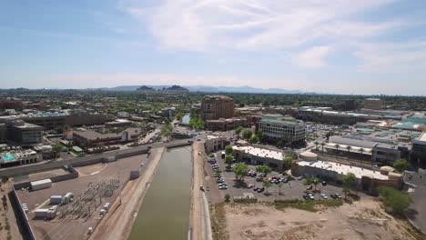 Aéreo-Lento-Push-up-Arizona-Canal-Trail-Hasta-El-Centro-Del-Casco-Antiguo-De-Scottsdale,-Camelback-Y-Scottsdale-Road