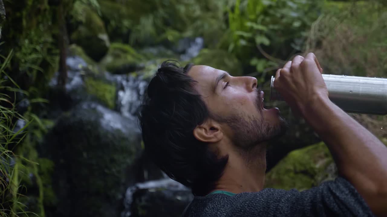 madeira, portugal - turista masculino bebiendo agua en su vaso en cámara lenta con un maravilloso paisaje de agua clara que fluye sobre las rocas - toma de primer plano