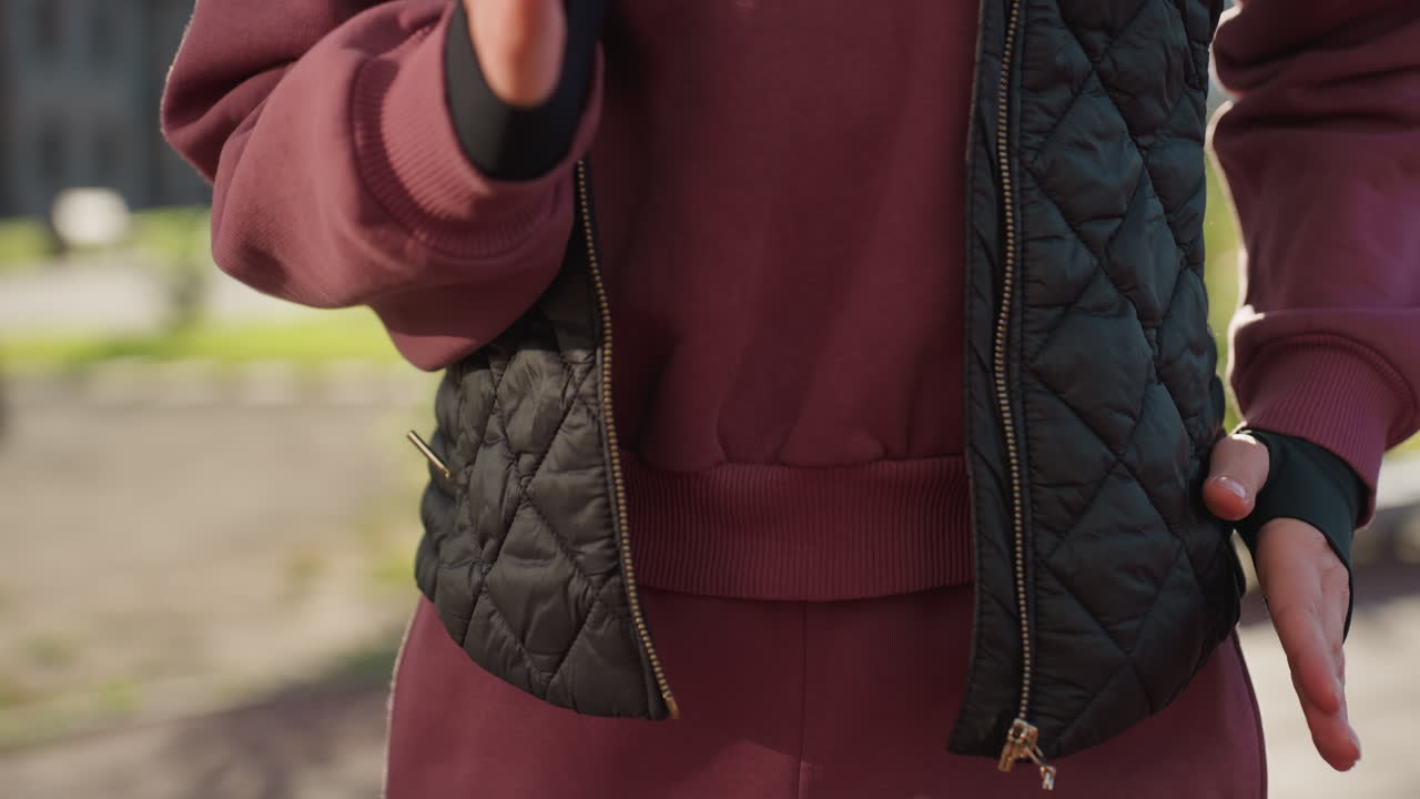 Lower view of trainer in hoodie and vest running on spot outdoors in urban park with fitness bars under sunlight, legs and hands moving dynamically as part of warm up fitness exercise session