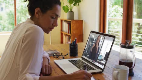 Mixed-race-businesswoman-sitting-at-desk-using-laptop-having-video-call-with-female-colleague