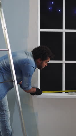 black employees measure window width with retractable tape in room at night. african-american colleagues renovate apartment together. checking size