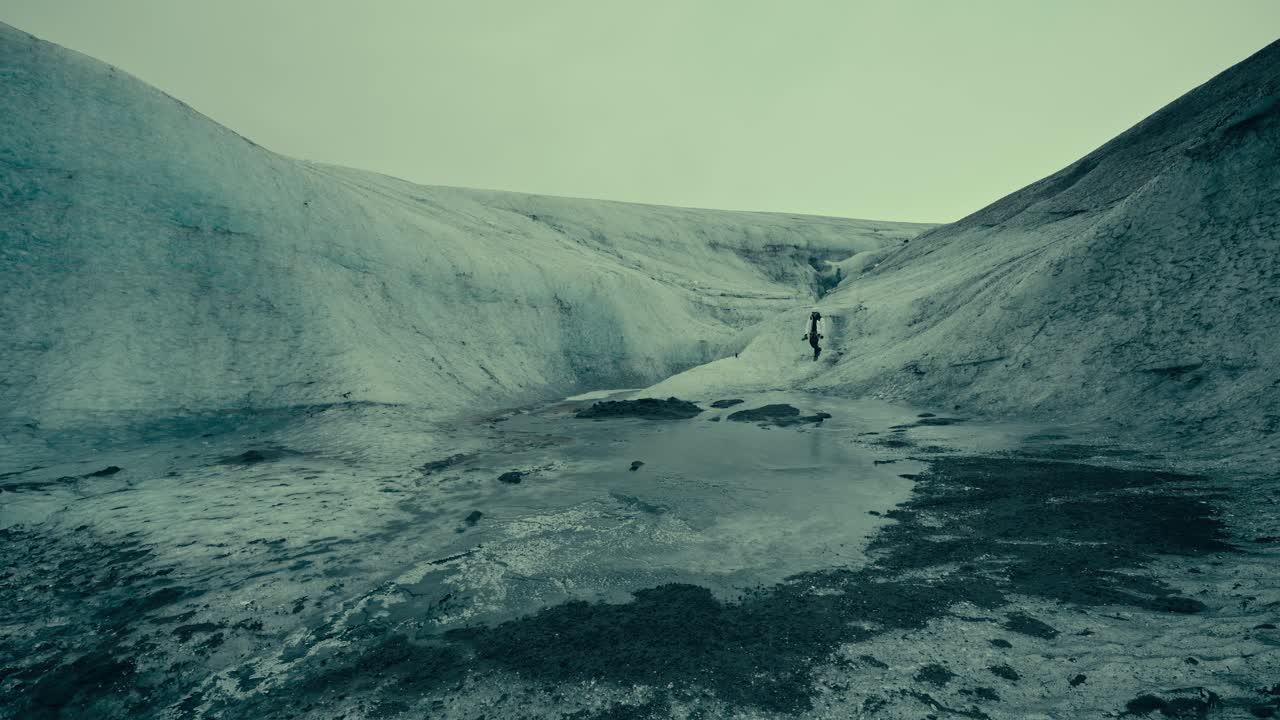 Persona che cammina su un vasto paesaggio glaciale con acqua di scioglimento.