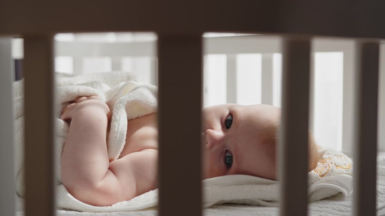 Newborn baby wrapped in soft towel lying in crib with sunlight streaming through bars a baby newborn