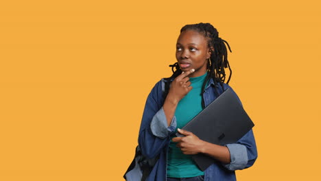 pensive woman carrying laptop, doing thinking gesture, studio background
