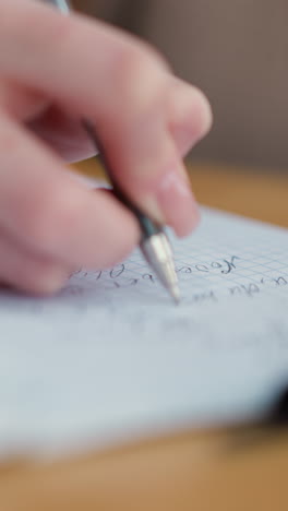 primer plano de un estudiante tomando notas en un cuaderno con una pluma en un paño tejido colocado en una mesa de madera, actividad de escritura enfocada con iluminación suave y superficie natural de madera