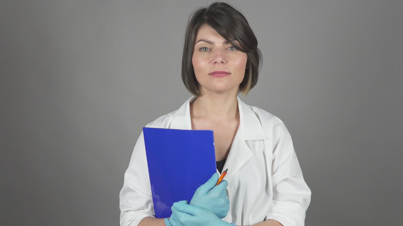 Friendly young nurse holding folder isolated on grey background. Healthcare concept. Shot in 4k.