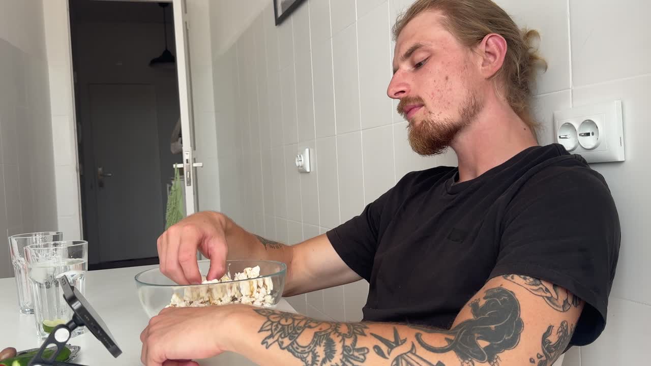 Joven con tatuajes comiendo palomitas de maíz en casa
