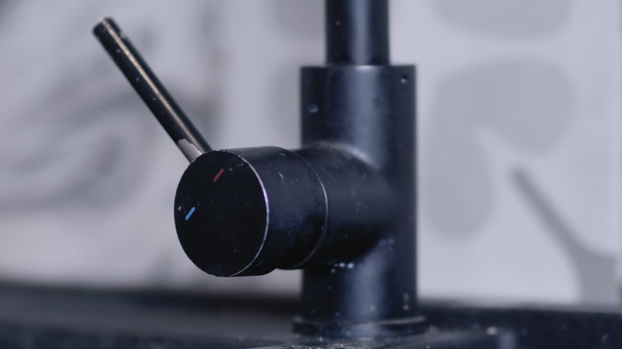 Cold water tap is turned off at the lever by a man's hand in a modern grey tiled kitchen.