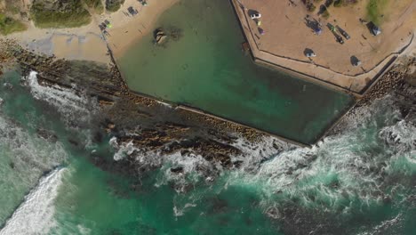 high aerial rotating view of an ocean rock pool with people swimming