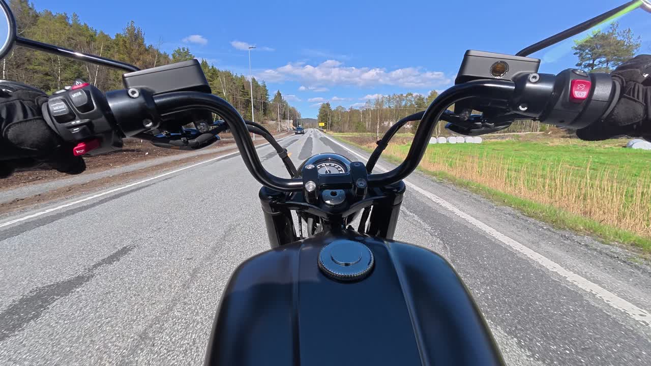 POV ripresa con action camera montata sul petto di una motocicletta da turismo su una strada liscia e rettilinea in Norvegia durante l'estate. Alberi verdi e paesaggi di campagna sfilano via, catturando un rilassante viaggio on the road, f